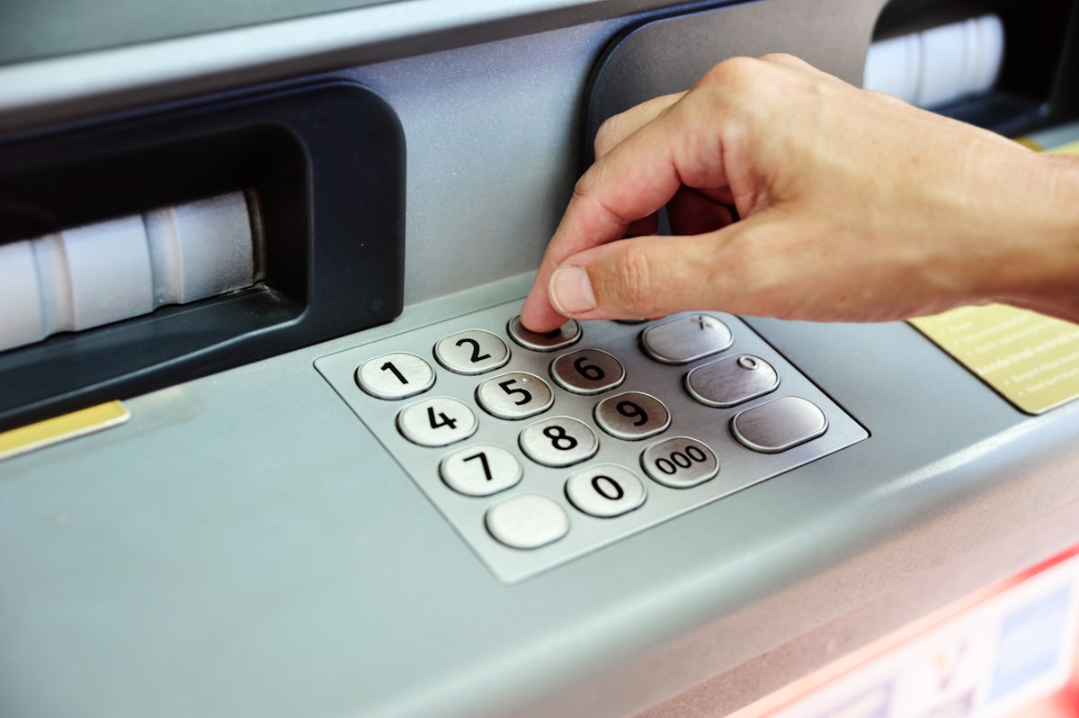 A hand pressing the numbered metal keypad on a bank cash machine