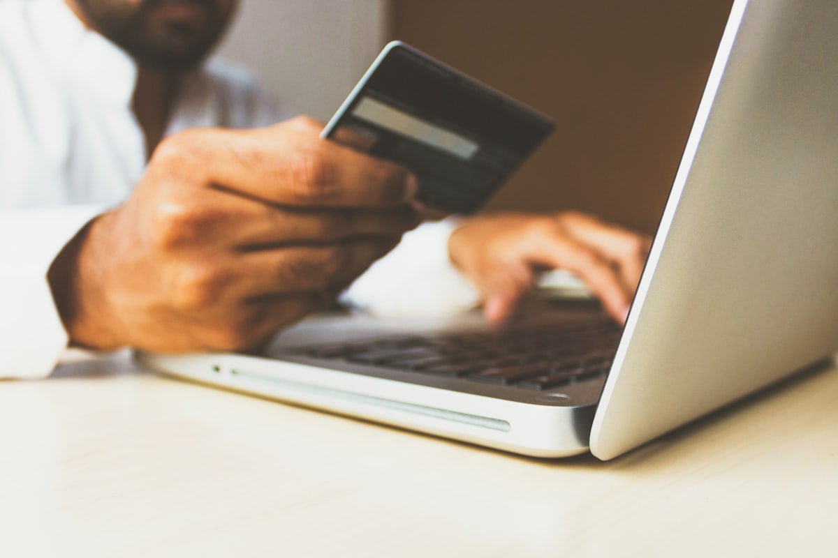 A person holding a payment card in front of a laptop while shopping online
