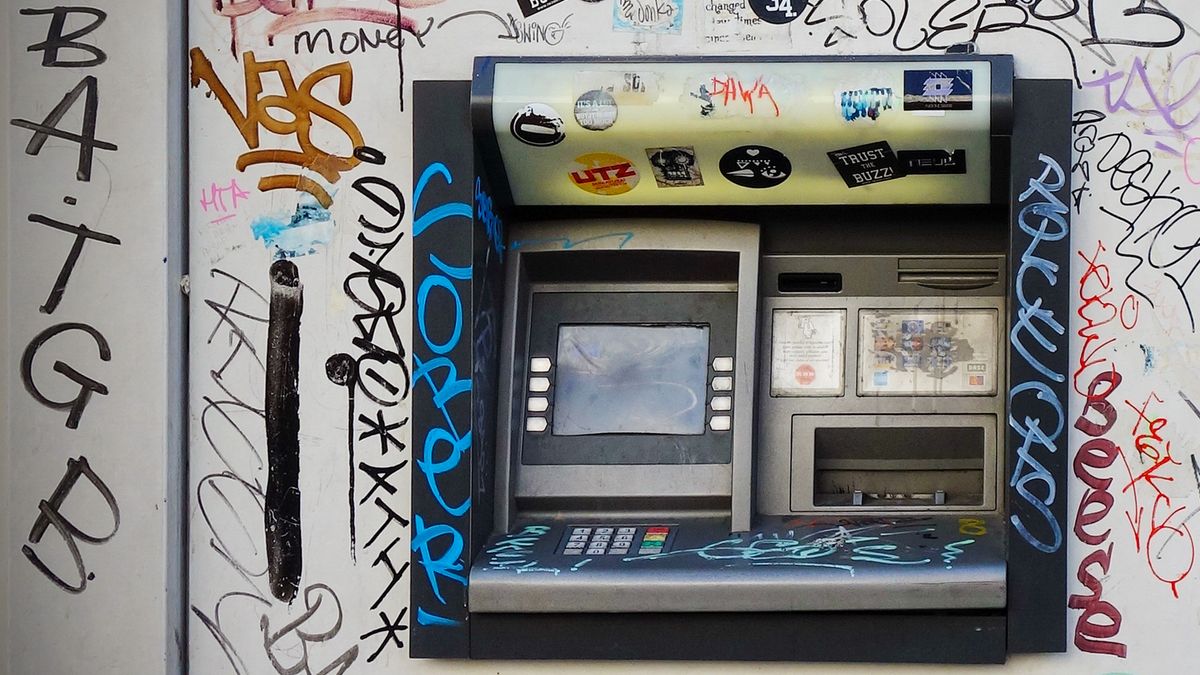 A standalone street ATM covered in graffiti and stickers